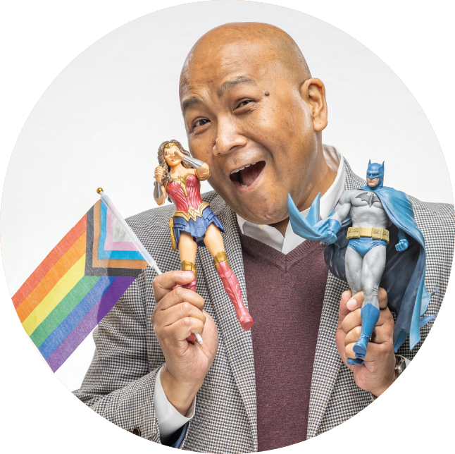 Wally holding a Pride flag, and a batman and wonder woman figurines.
