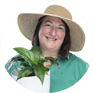 Headshot of DeeAnn Jurgens wearing a gardening hat, holding a plant.